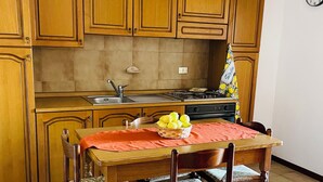A kitchen with wooden cabinets, a dining table with chairs, a fruit bowl, and a clock on the wall. - Family House San Marco – A Warm Welcome Near Taormina and Mount Etna. (Calatabiano)