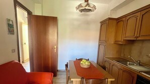 A compact kitchen with wooden cabinets, a dining table with chairs, and a red sofa. - Family House San Marco – A Warm Welcome Near Taormina and Mount Etna. (Calatabiano)
