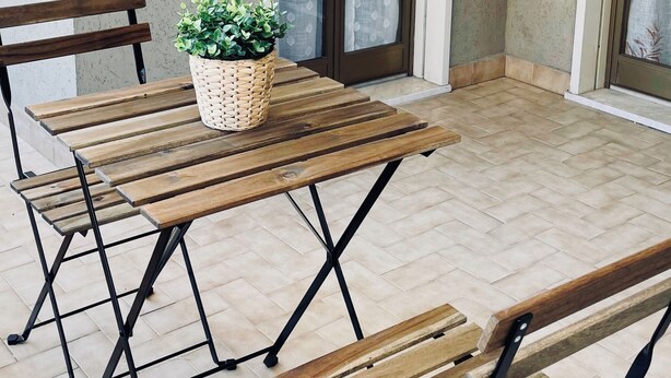 A patio with a wooden table and benches, a potted plant, and a sliding glass door with curtains. - Family House San Marco – A Warm Welcome Near Taormina and Mount Etna. (Calatabiano)