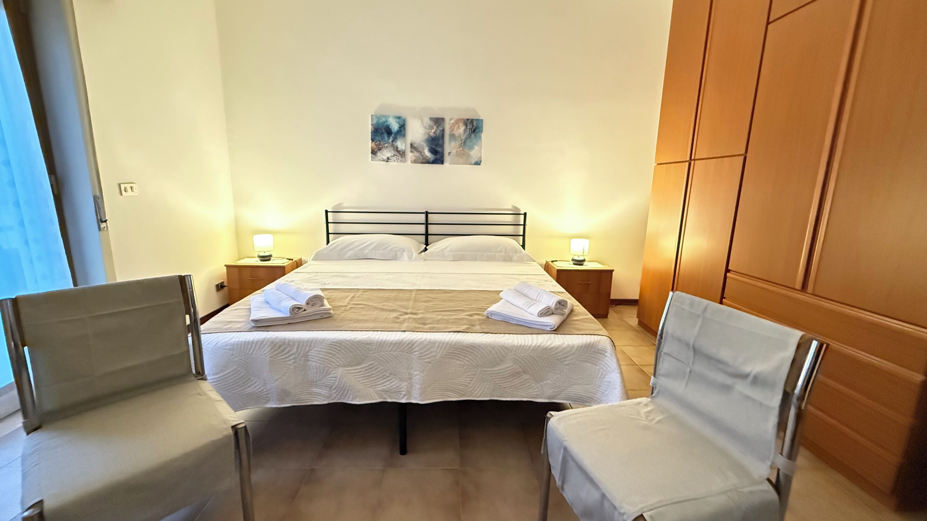 Une chambre d’hôtel comprenant un lit, deux tables de chevet avec des lampes, une chaise et une armoire.