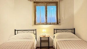 A room with two beds, a window with curtains, a lamp on a bedside table, and a ceiling light. - Family House San Marco – A Warm Welcome Near Taormina and Mount Etna. (Calatabiano)