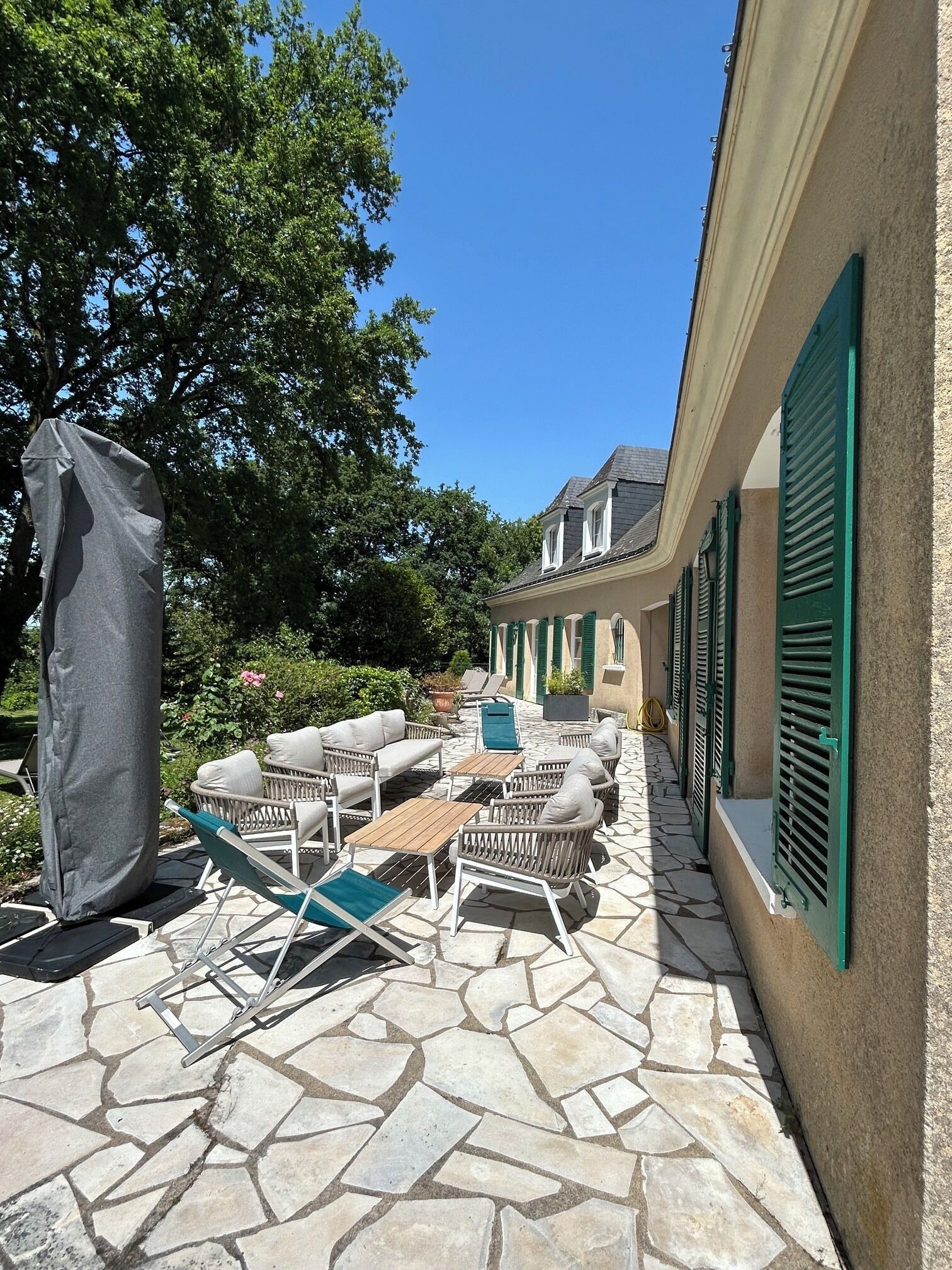 Une terrasse extérieure avec un sol en pierre, des meubles en osier et une statue abritée.