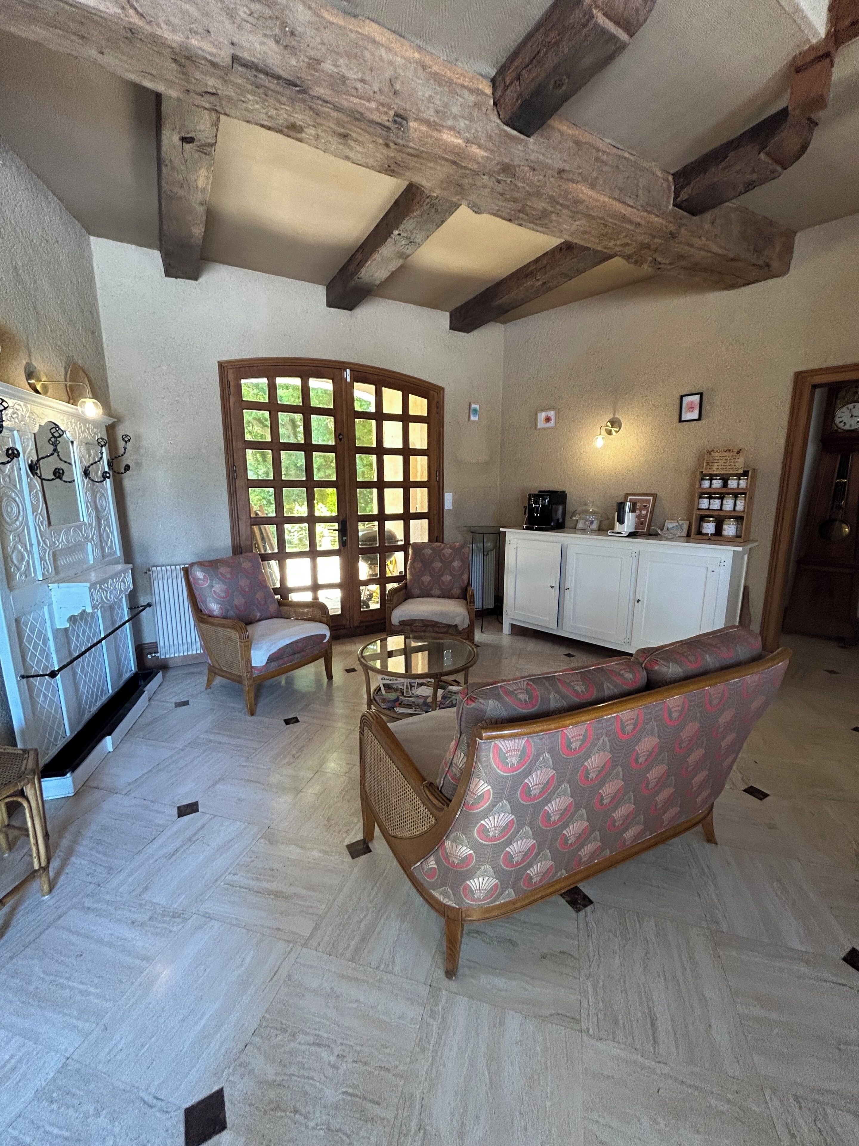Una habitación amplia con techo alto, vigas de madera, un gran ventanal y un área de descanso con sofá y sillas.