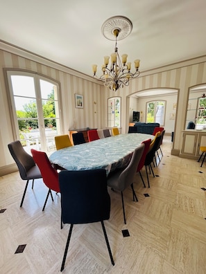 A dining area with a large table, chairs, a chandelier, and a view of the outdoors. - GRAND GITE LA MONERIE, for your stays with family, friends, or for business (Segré-en-Anjou Bleu)