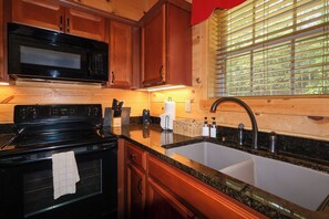 A kitchen with wooden cabinets, a black microwave, a stove, and a sink with a faucet. - Firepit, hot tub, sleeps 7, exclusive hiking for resort, volleyball, peaceful! (Sevierville)