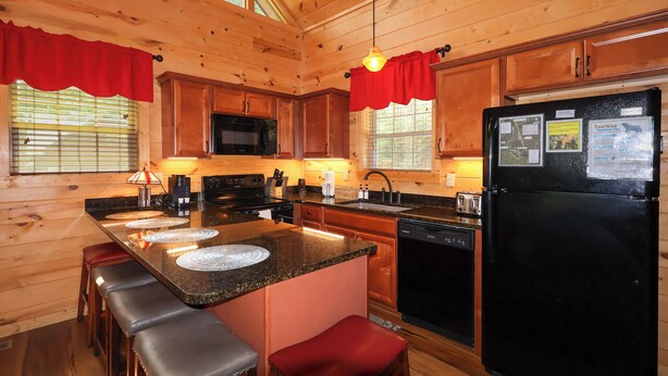 A wooden cabin kitchen with a central island, a black refrigerator, and wooden cabinets. - Firepit, hot tub, sleeps 7, exclusive hiking for resort, volleyball, peaceful! (Sevierville)