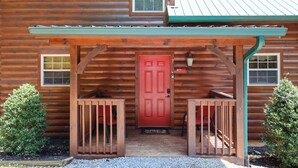 A log cabin with a red door, two wooden benches, and a covered porch. - Firepit, hot tub, sleeps 7, exclusive hiking for resort, volleyball, peaceful! (Sevierville)
