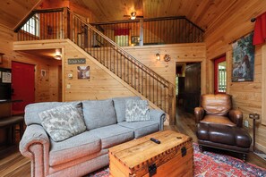 A wooden interior with a sofa, a leather chair, a wooden chest, and a staircase. - Firepit, hot tub, sleeps 7, exclusive hiking for resort, volleyball, peaceful! (Sevierville)