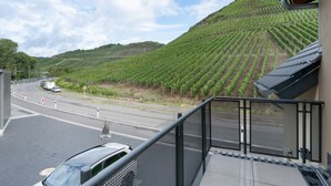 A balcony with a view of a vineyard and a road with vehicles.