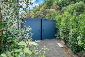 Ein blauer Metallschuppen in einem Garten mit einem gepflasterten Weg, der dorthin führt.