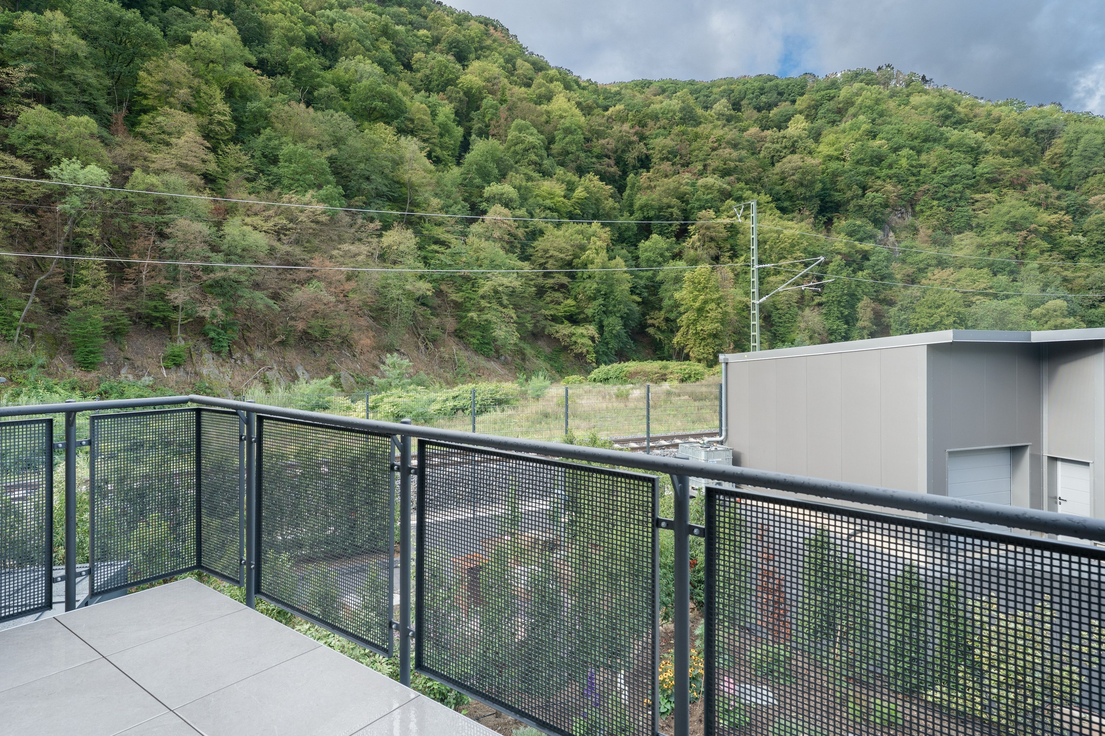 Ein Balkon mit Metallgeländer mit Blick auf eine bewaldete Hügelkuppe.