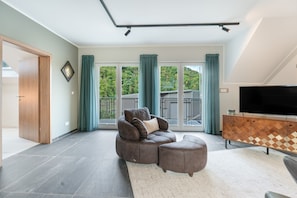 A modern living room with a sectional sofa, a flat-screen TV, and a large sliding glass door leading to a balcony.