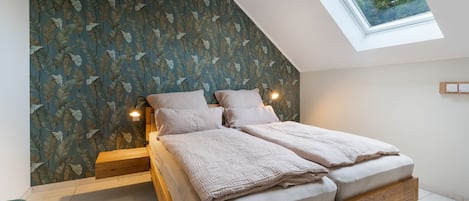A bedroom with a sloped ceiling, a skylight, a bed with a wooden frame, and a wall with a leaf pattern.
