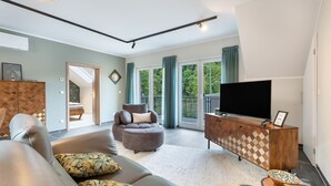 A modern living room with a sofa, armchair, and ottoman, a television, and a wooden cabinet.
