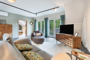 A modern living room with a sofa, armchair, and ottoman, a television, and a wooden cabinet.