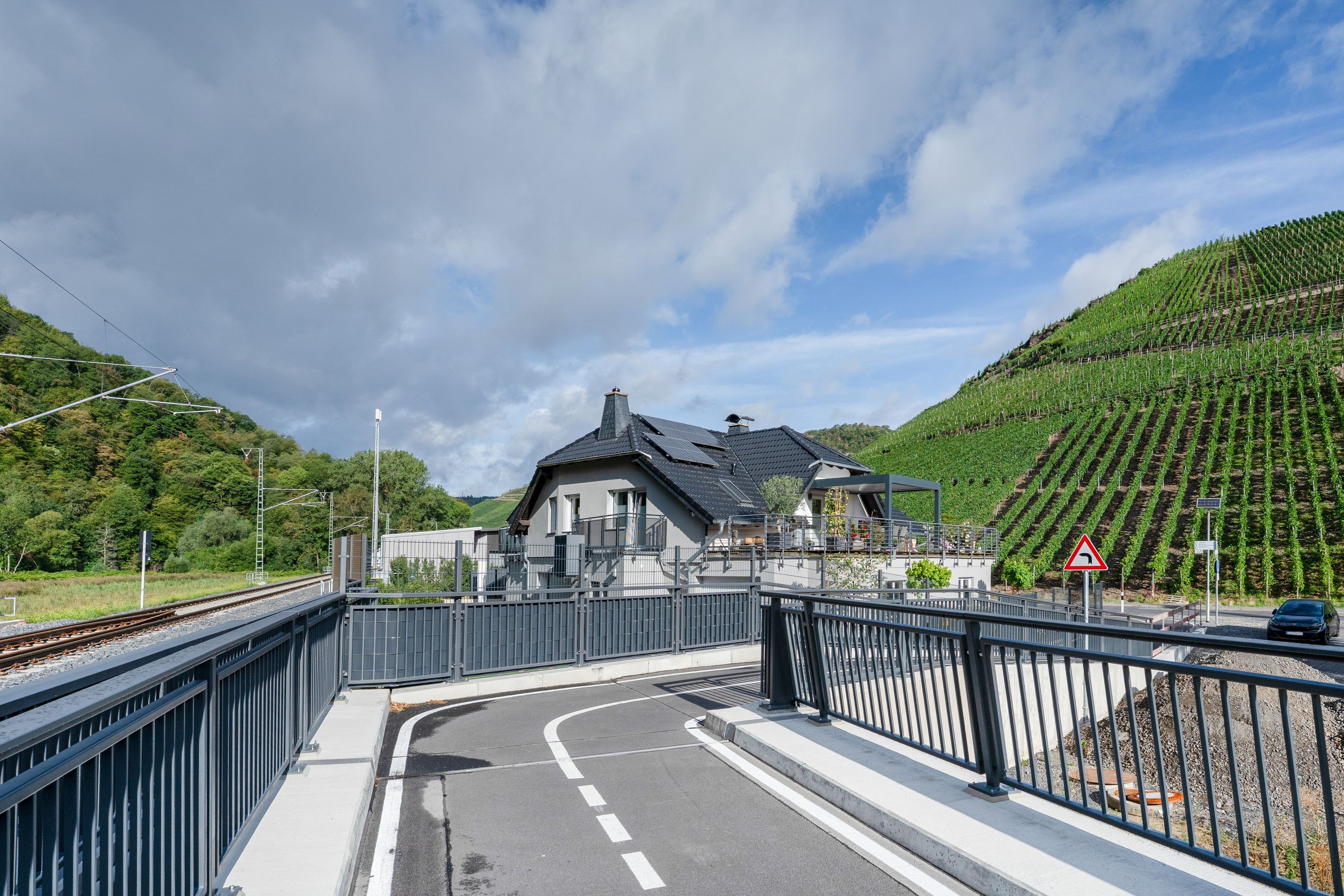 Ein Bahnübergang mit einem Haus und einem Weinberg im Hintergrund.