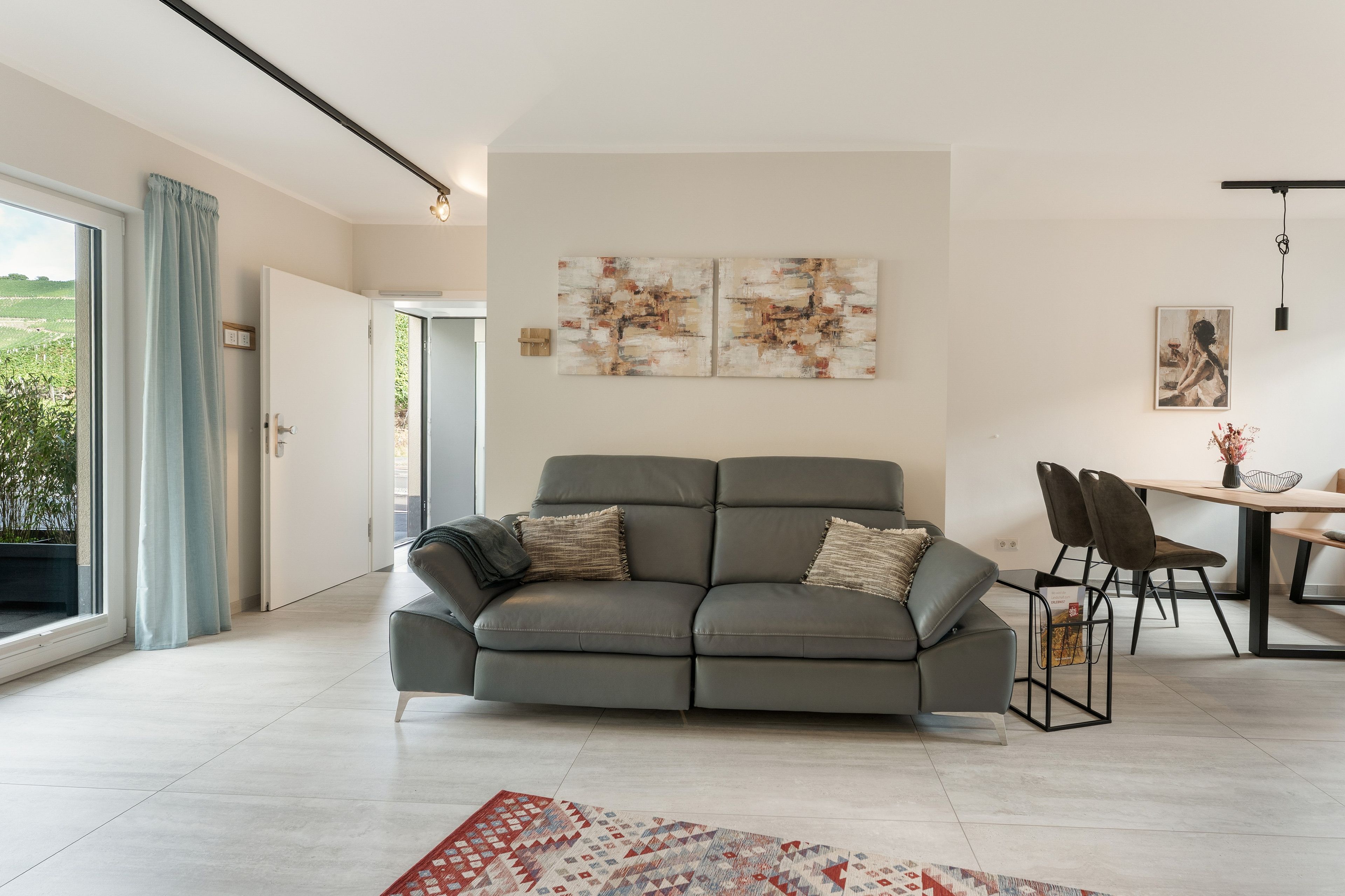 Een moderne woonkamer met een grijze bank, een eettafel met stoelen en kunstwerken aan de muur.