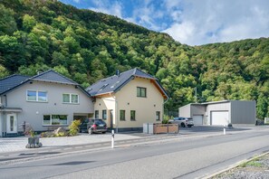 A residential area with two houses, a paved road, and a forested hillside.