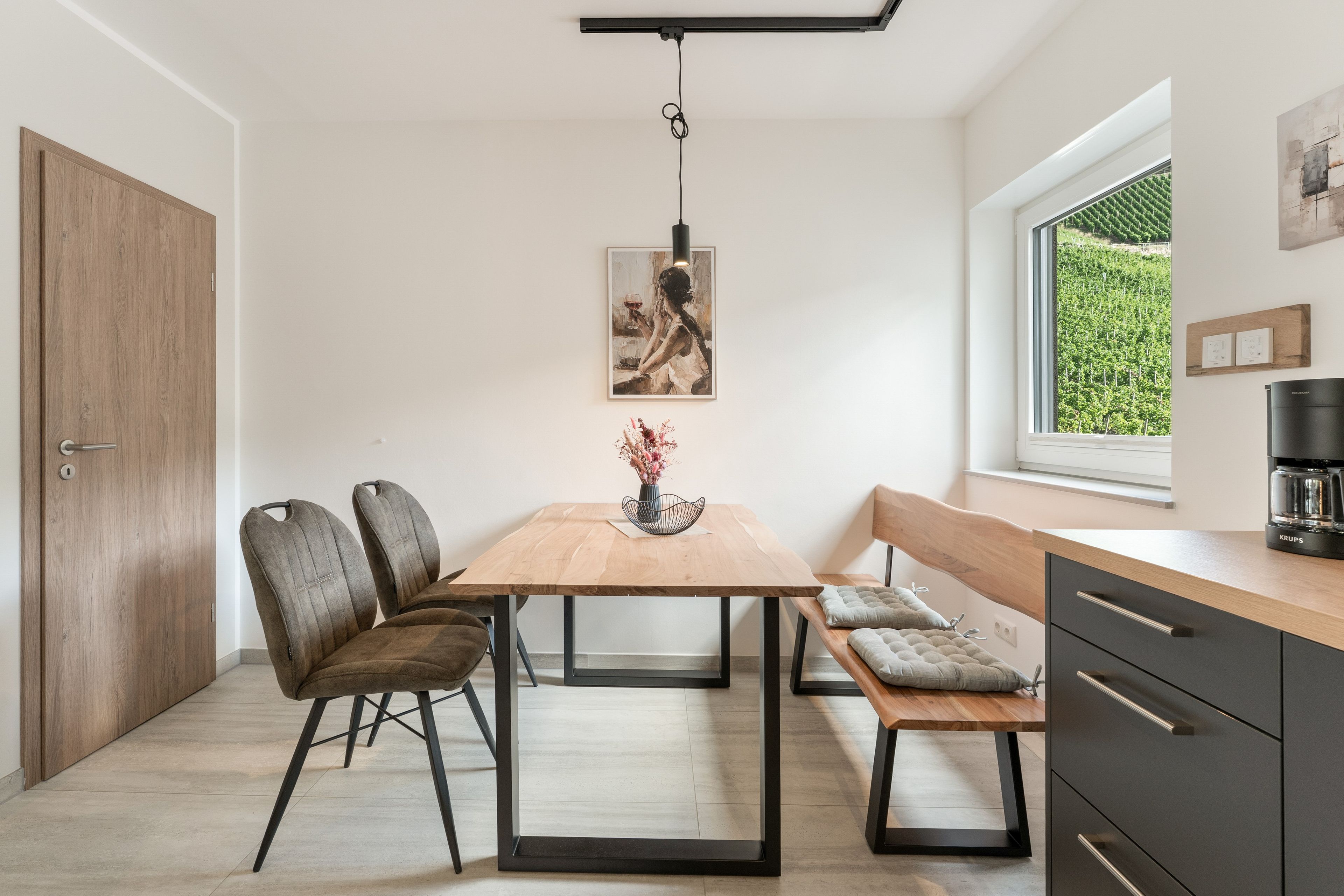 Eine moderne Küche mit einem Holztisch, Stühlen, einer Bank und einer Kaffeemaschine.
