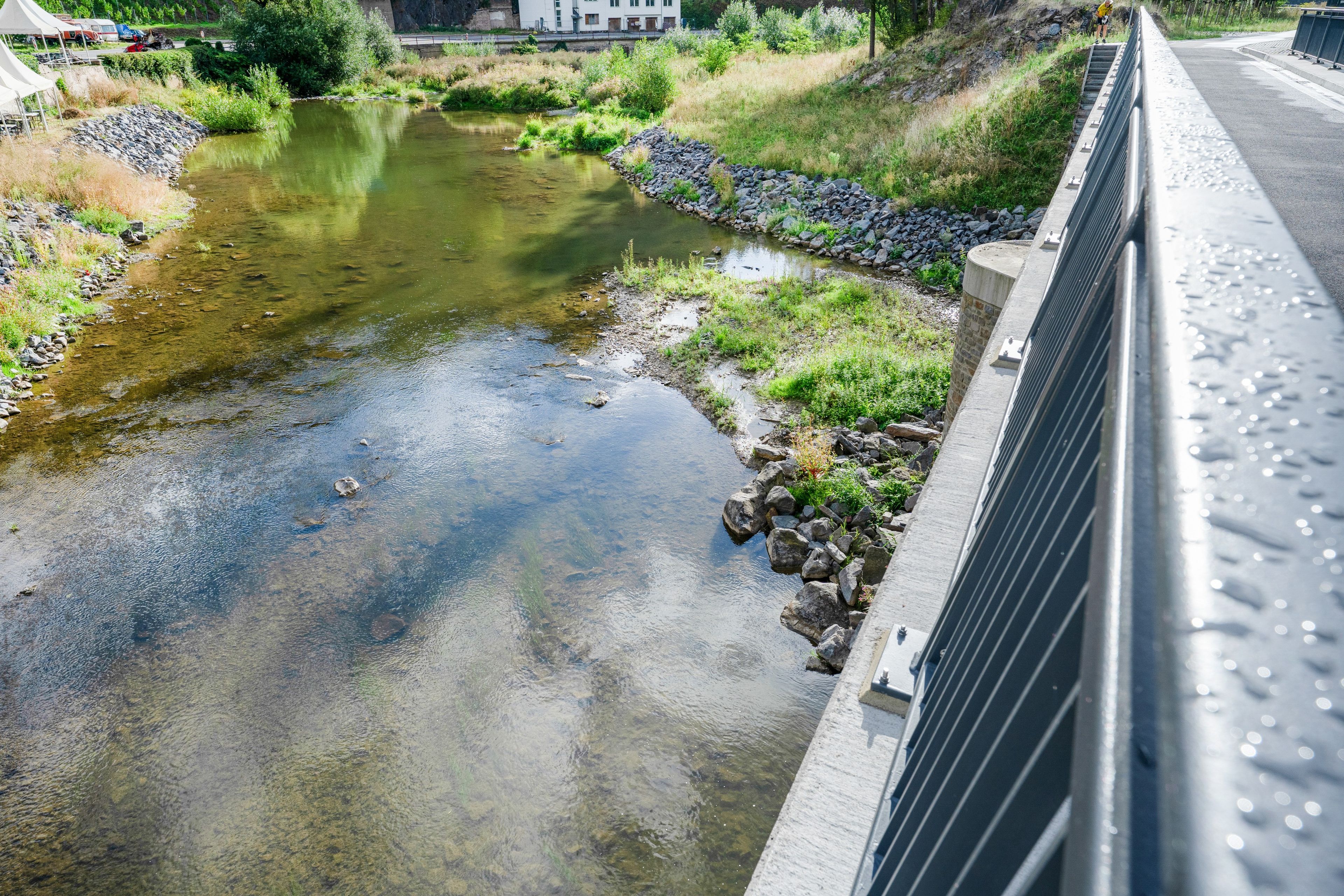 Een rivier met helder water, omgeven door begroeiing en een betonnen muur.