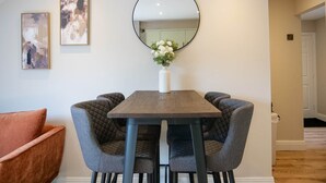 Un coin repas agrémenté d’un miroir rond, de deux œuvres d’art encadrées et d’un vase avec des fleurs posé sur une table.