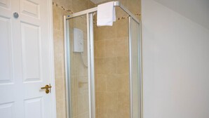 Une douche fermée par des parois de verre, avec une serviette blanche accrochée à la poignée de la porte.