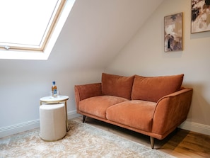 A cozy room with a sloped ceiling, a brown sofa, a small round table with glasses, and a white ottoman. - Town Central Nest - Dingle (Dingle)