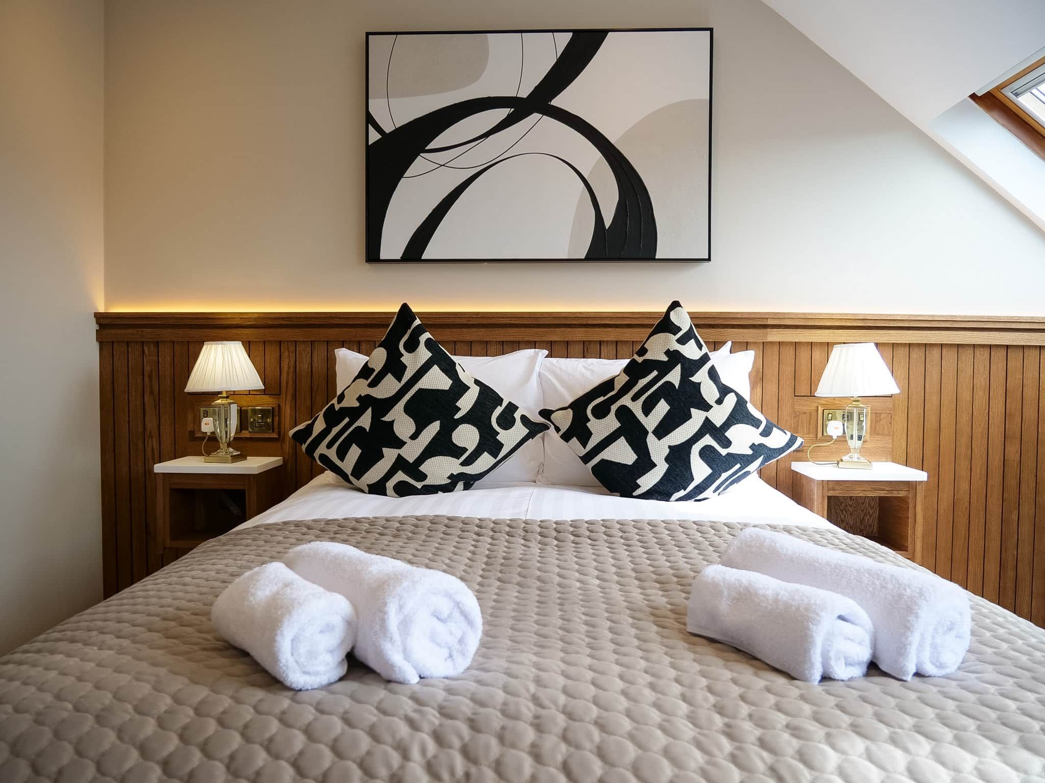 Una habitación de hotel con una cama, dos mesitas de noche, un cuadro abstracto colgado en la pared y una ventana.