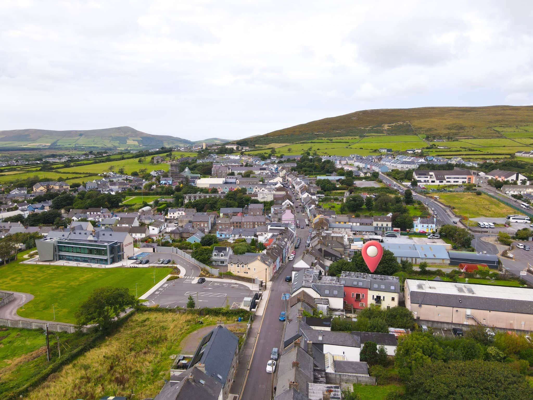 A town with a mix of residential and commercial buildings, a main road, and surrounding green fields.