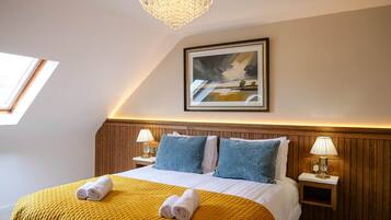 A hotel room with a bed, a painting, a chandelier, and a window.