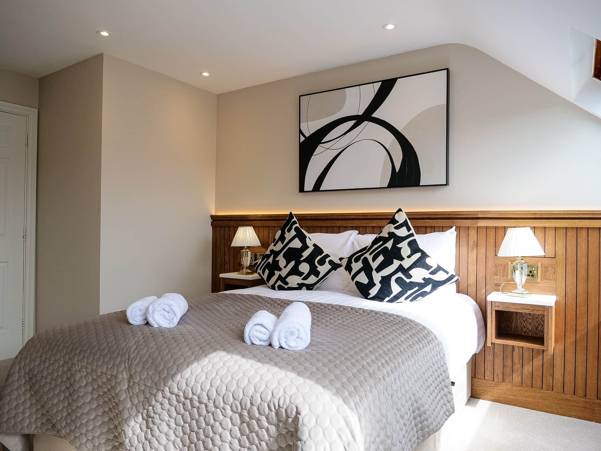 A hotel room with a large bed, two bedside tables, a wall-mounted abstract painting, and a wooden headboard.