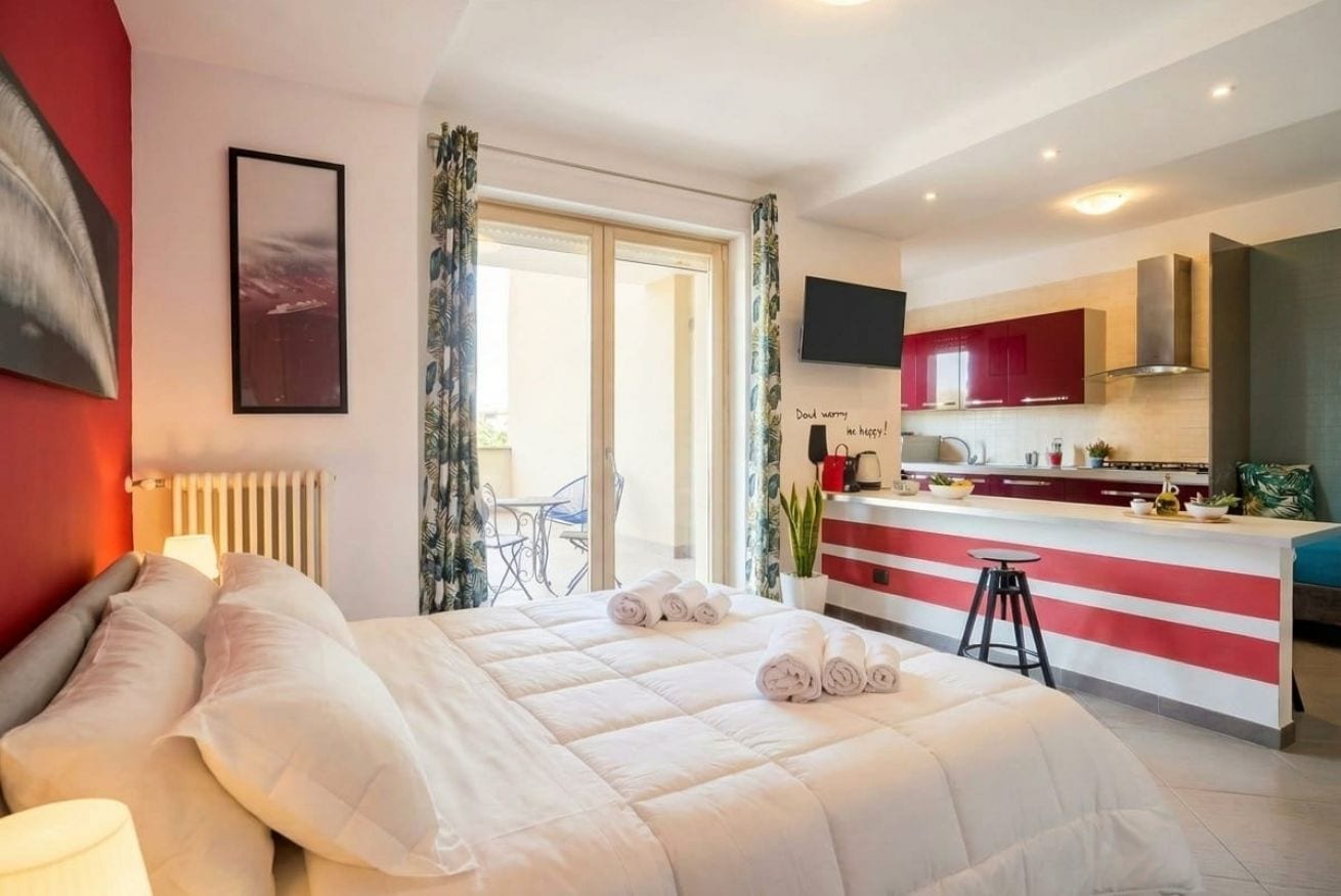 A hotel room with a bed, a desk, a kitchen area, and a view of the outdoors.