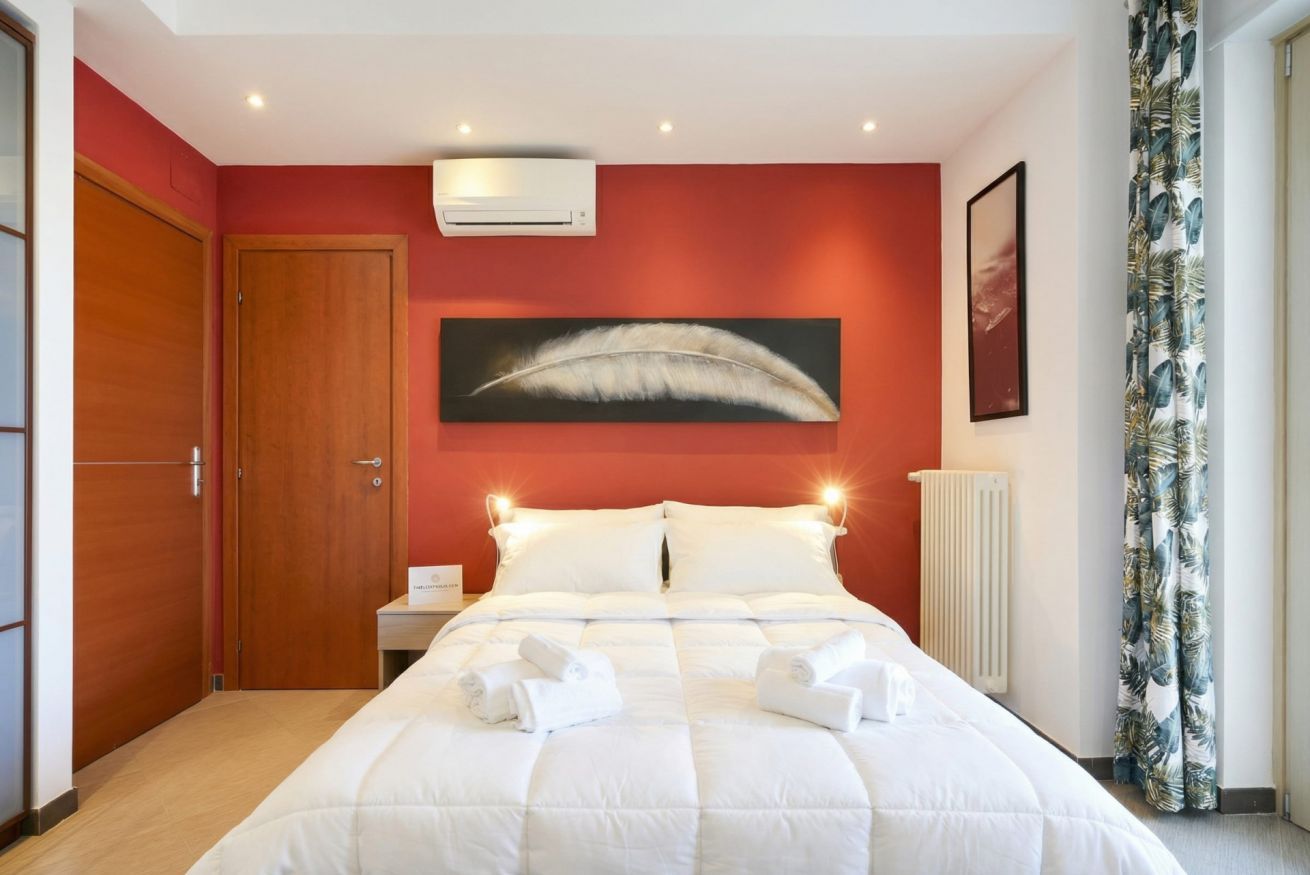 Ein Hotelzimmer mit einem Bett, einer Wand-Klimaanlage, einer gerahmten Feder-Kunstarbeit, einem gerahmten Bild und einem Vorhang mit Blätermuster.