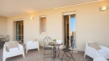 A balcony with white chairs, a small table with a plant, and a view of the interior through open doors.