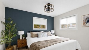 Ett sovrum med en säng, sängbord, en lampa, en växt och ett fönster.