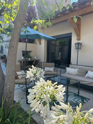 Ein Außenbereich mit Sitzgelegenheiten, darunter eine Couch, Stühle und ein Tisch, sowie ein Blumentopf mit weißen Blüten.