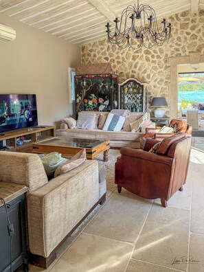 Un salon avec un mur en pierre, un téléviseur, un canapé, une table basse et un lustre.