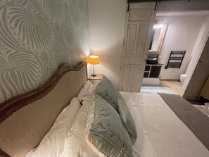 A bedroom with a bed, a nightstand with a lamp, a patterned wall, and a view into the bathroom. - COTE D'AZUR - 4-BEDROOM, AIR-CONDITIONED STONE BASTIDE WITH POOL - SLEEPS 8 (Mougins)