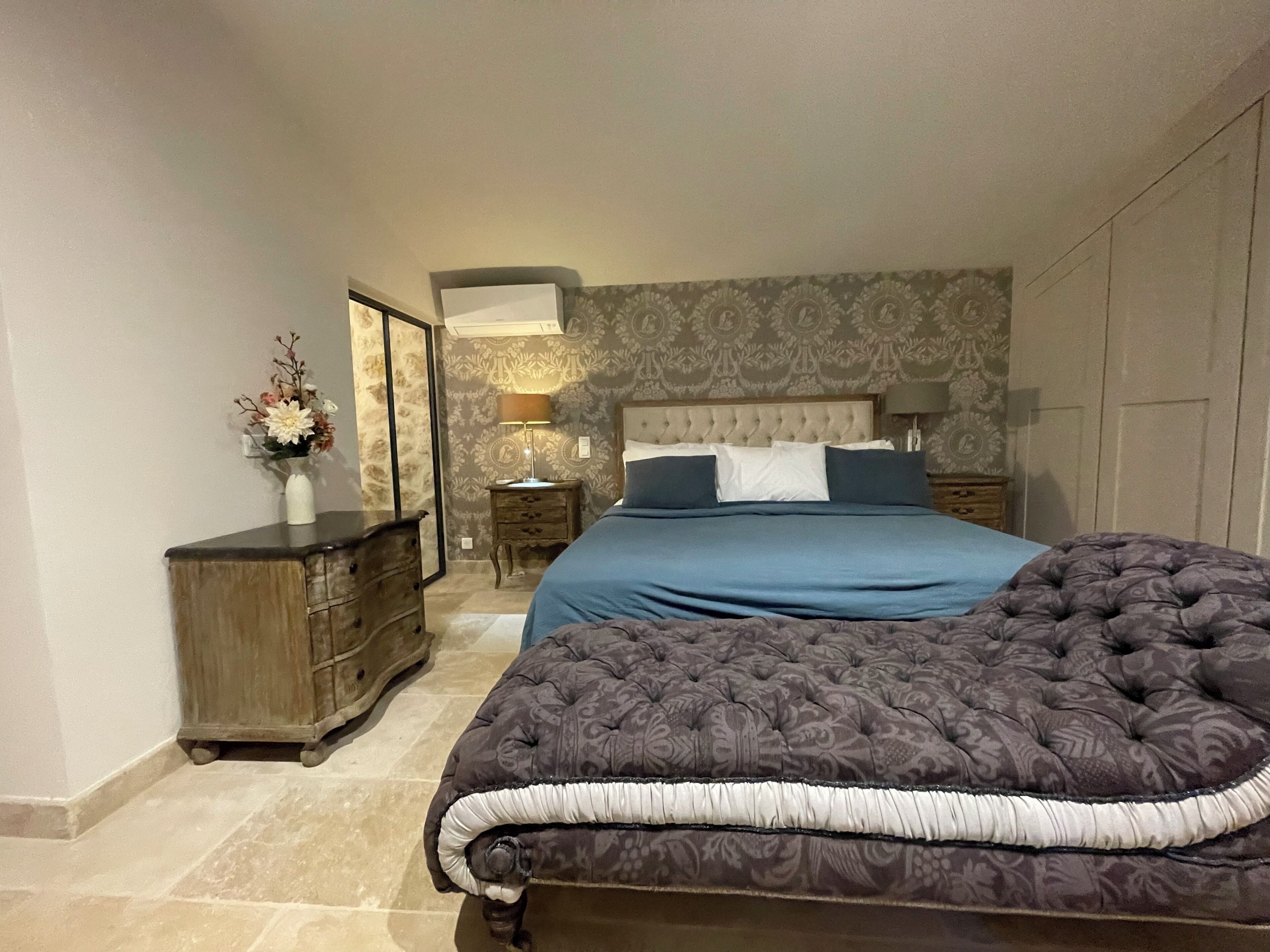 A bedroom with a large bed, a dresser, a nightstand, and a lamp.