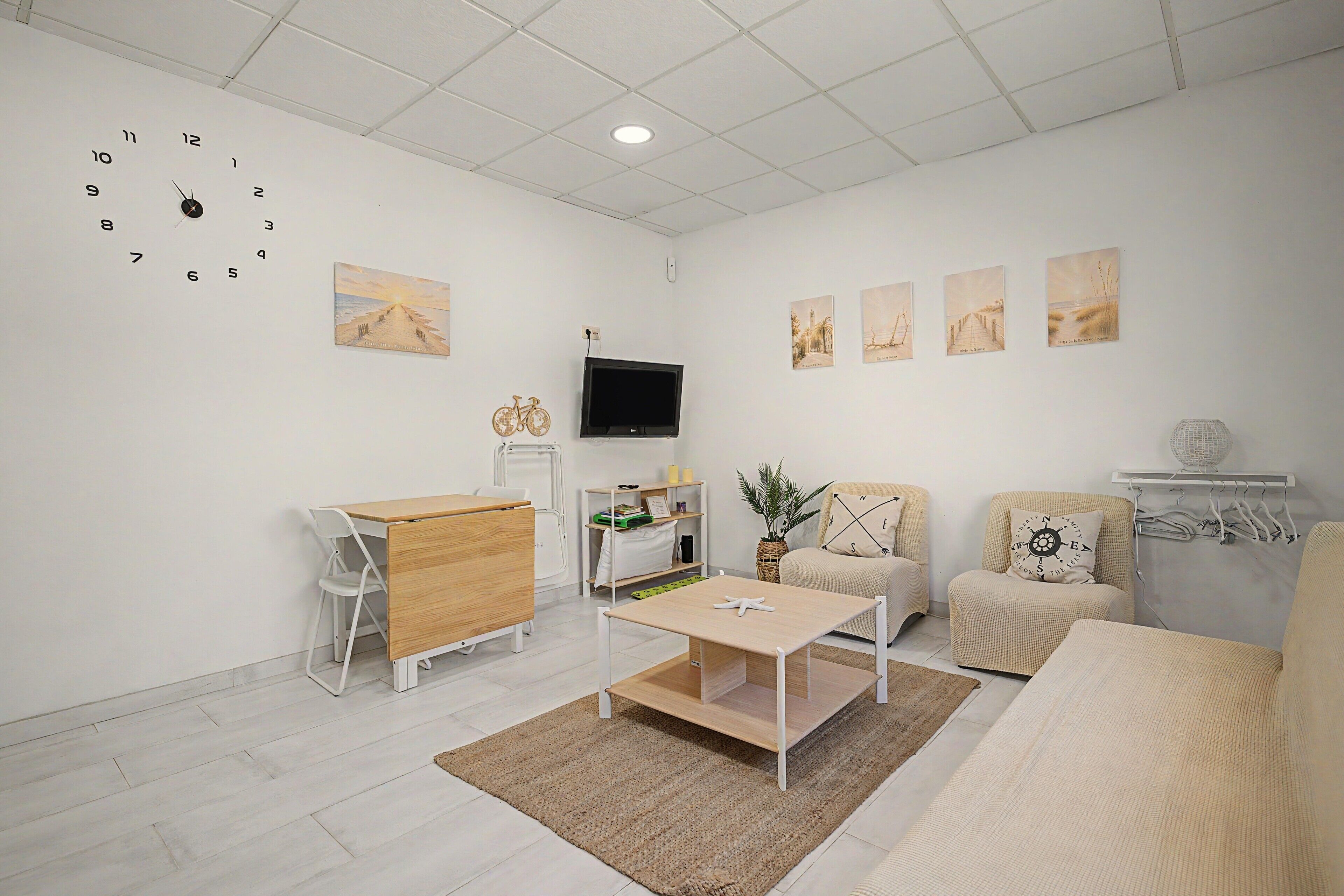 A modern living room with a wooden coffee table, a sofa, a TV mounted on the wall, and a series of framed artworks.