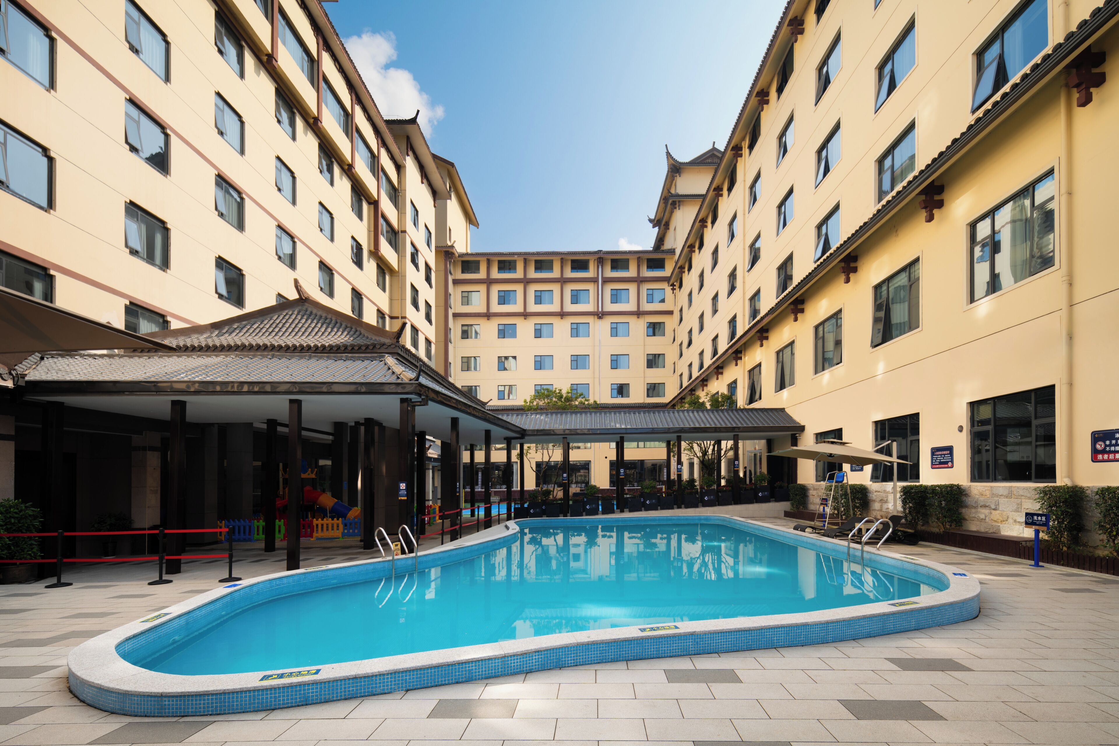 A hotel courtyard with a swimming pool, covered seating area, and multiple hotel buildings.