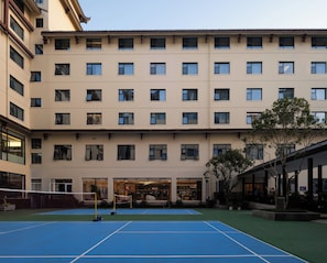 A multi-story building with a tennis court in the foreground.