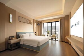 A hotel room with a bed, bedside table, a small table with chairs, a large window with a view, and a wall-mounted screen displaying hotel branding. - Zhangjiajie National Forest Park Renjoy (Zhangjiajie)
