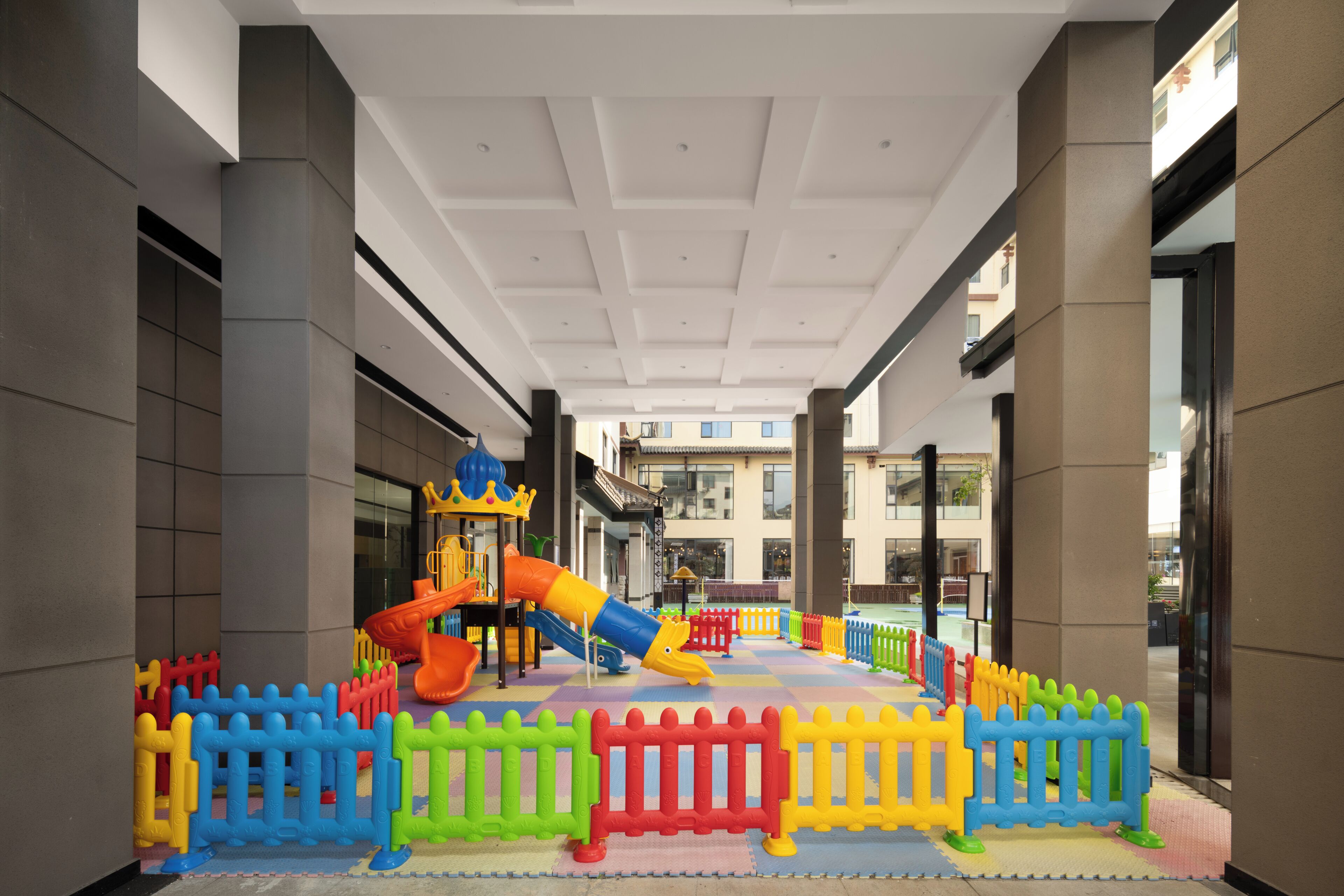 En lekplats för barn med rutschkanor och en borgliknande konstruktion, omgiven av färgglada staket.