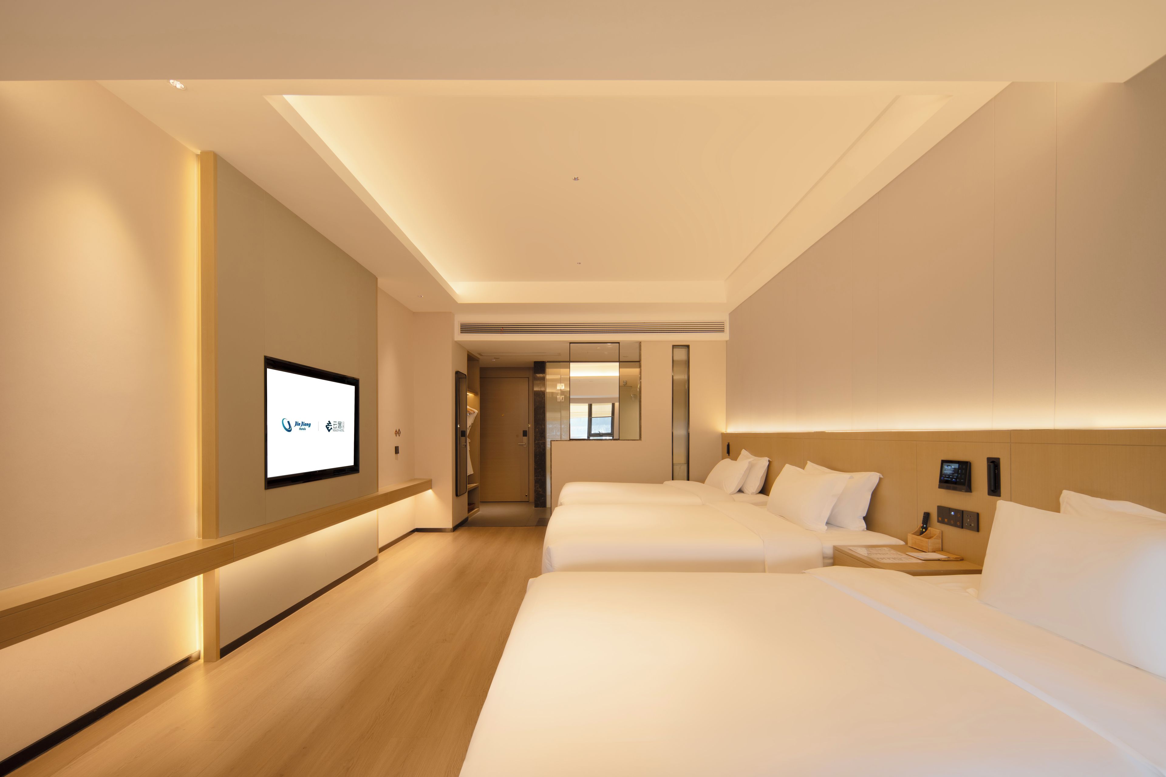 Een hotelkamer met een groot bed, een kleiner bed, een bureau met een lamp en een televisie aan de muur.