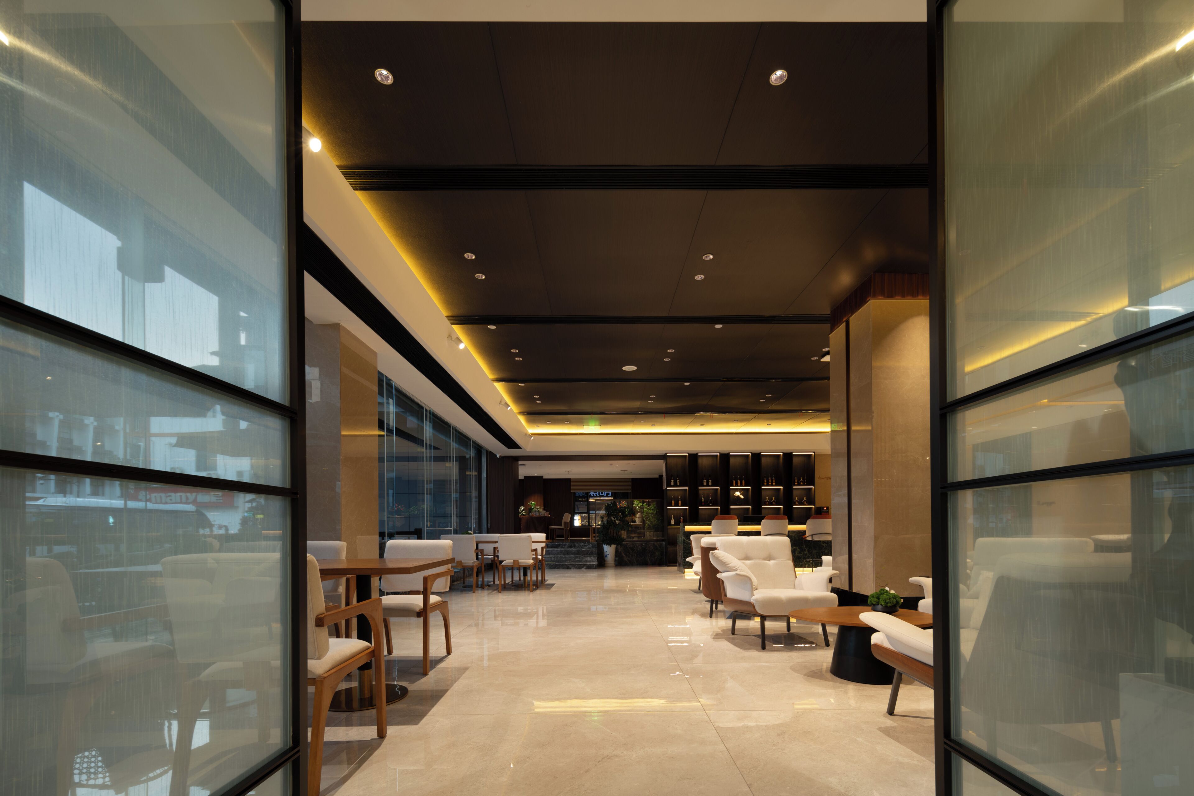 A modern hotel lobby with glass walls, seating areas, and a reception desk.