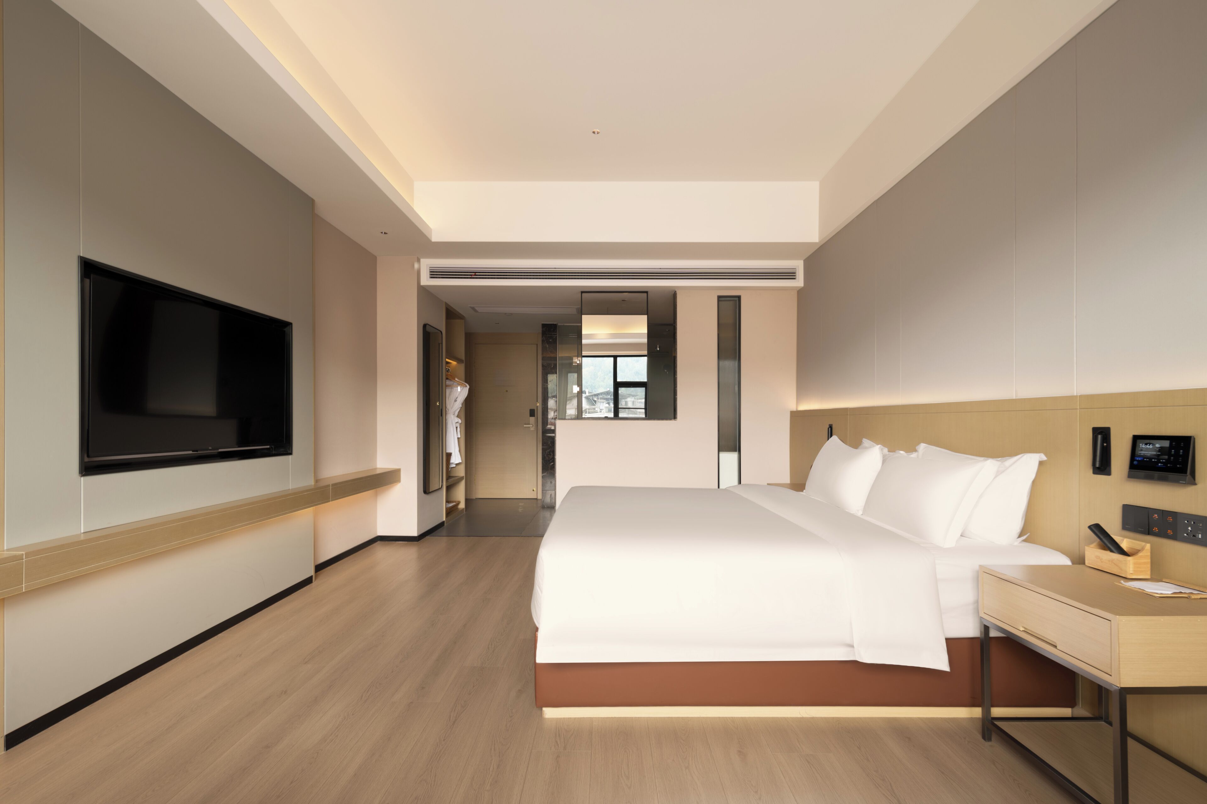 A modern hotel room with a large bed, a bedside table, a TV mounted on the wall, and a view of the hallway.