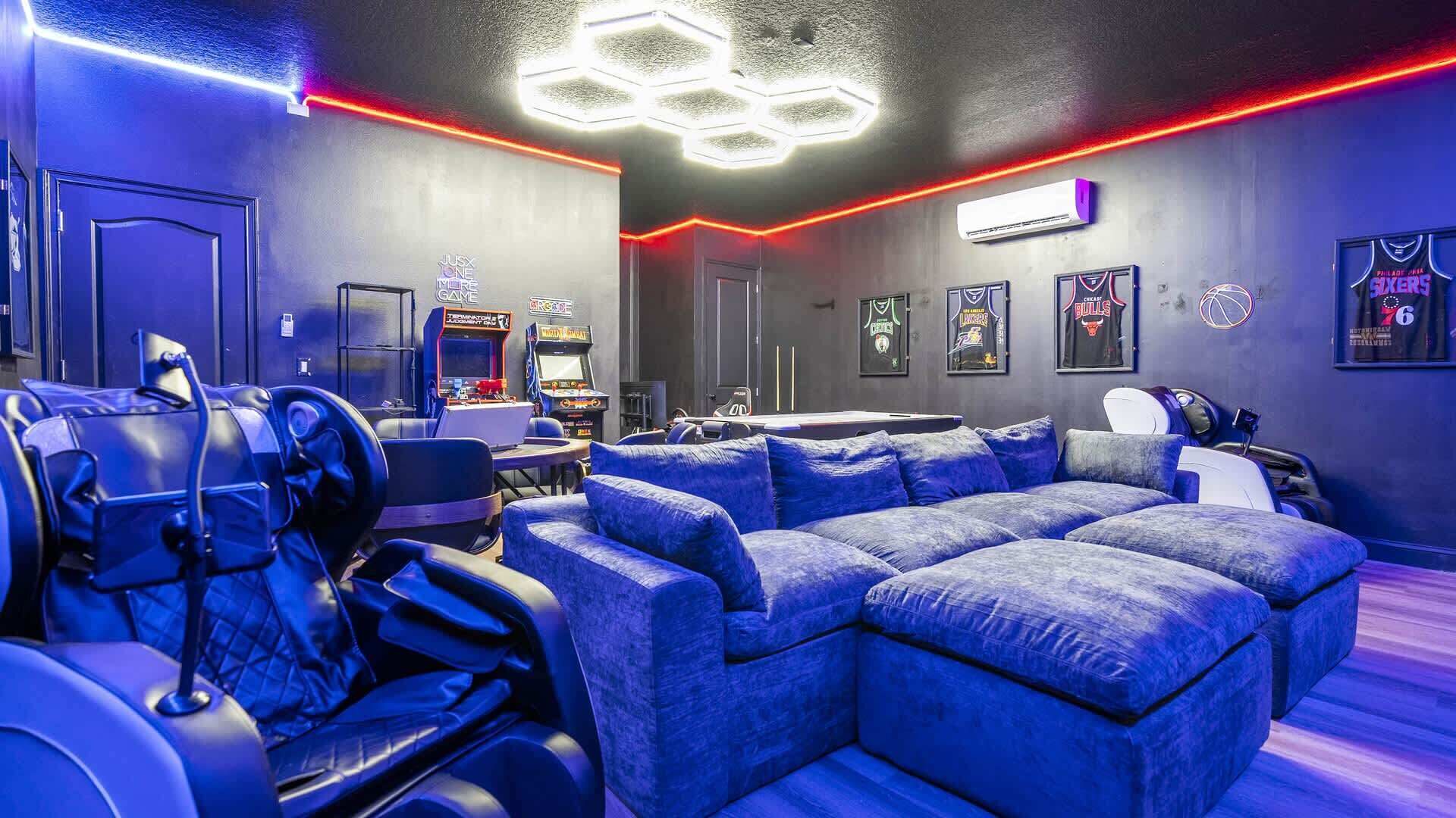 A room with a large sectional sofa, gaming consoles, and basketball memorabilia.