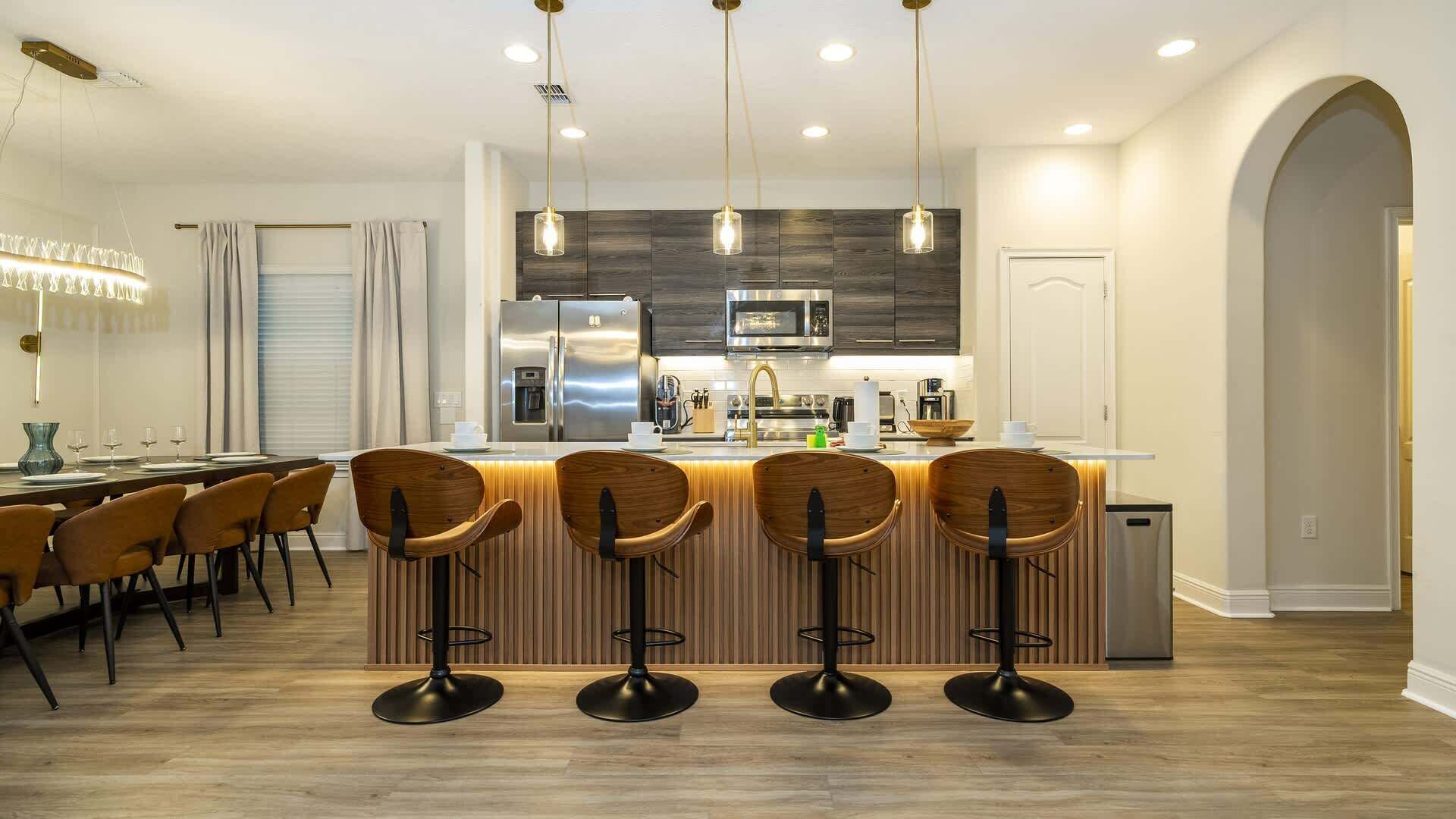 A modern kitchen with a central island, bar stools, and a dining area with a chandelier.