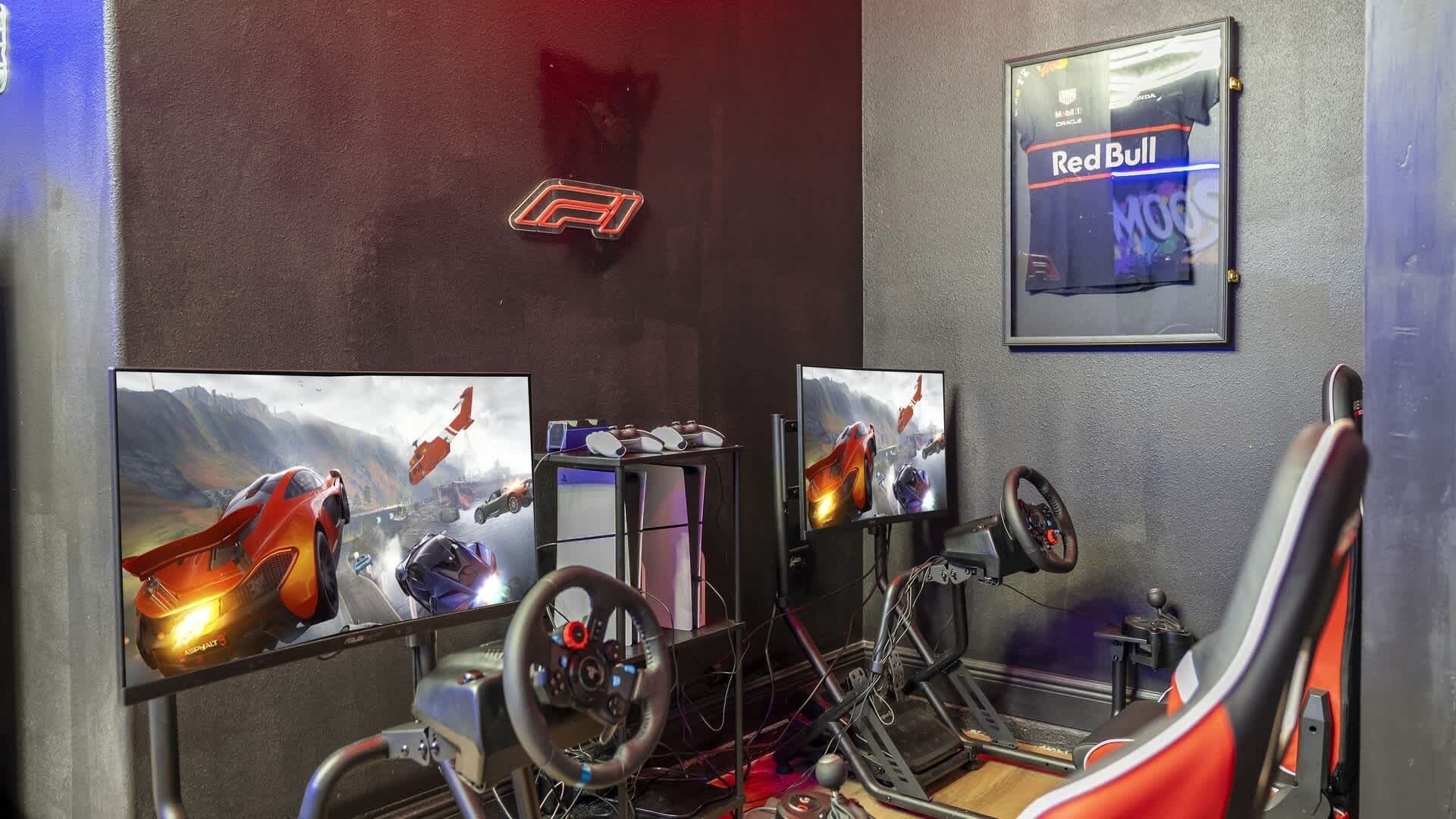 A gaming setup with multiple monitors, racing wheels, and a Red Bull sign on the wall.